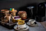 Handwoven traditional baskets holding Twinings Earl Grey tea, Nespresso capsules, and ceramic cups beside a modern coffee machine in guest room