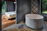 Freestanding soaking tub with ornate wallpaper and river views at The Namkhan riverside villa suite in Luang Prabang, Laos with open bedroom beyond