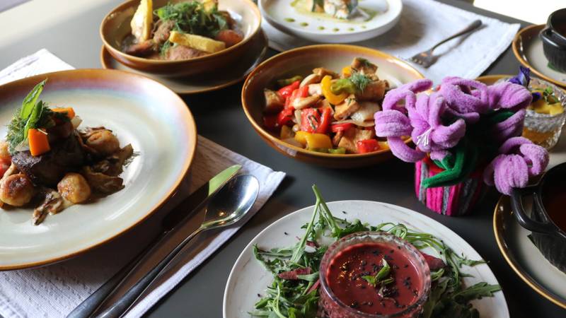 Colorful lunch spread at Namkhan restaurant featuring stir-fried vegetables, grilled meats, fresh salads with purple orchid garnish on ceramic plates