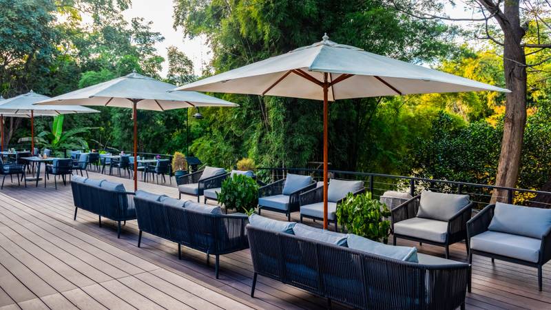 Outdoor restaurant deck with contemporary furniture, cream umbrellas, and lush jungle backdrop at Namkhan riverside dining terrace