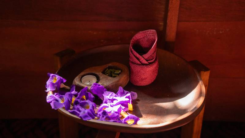 Purple orchids, rolled towel, massage stones and tea candle arranged on copper tray for in-room spa treatment at The Namkhan, Luang Prabang