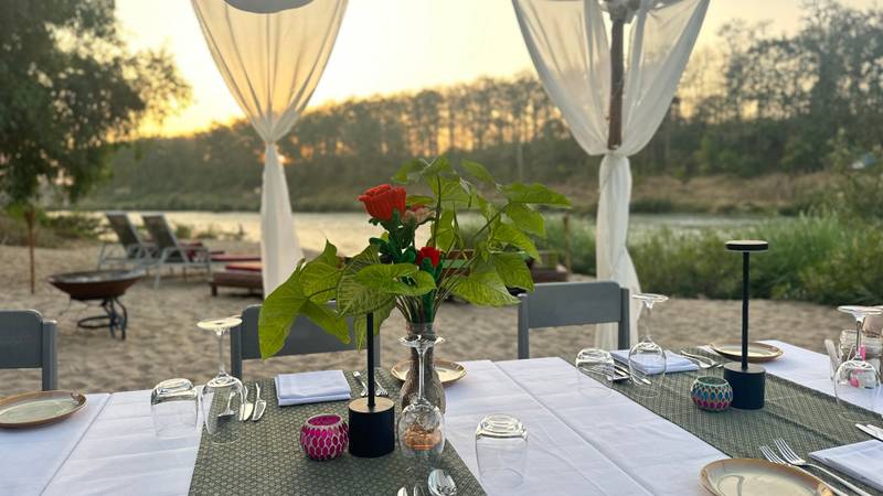Elegant riverside dining table set for dinner at The Namkhan resort in Luang Prabang, with sunset views over the Nam Khan river and jungle.