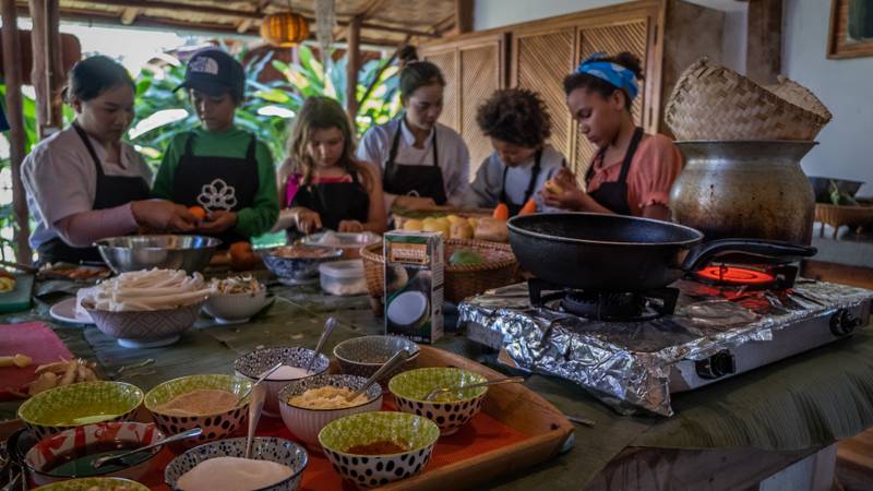 Guests preparing local dishes together in an open-air traditional kitchen with bamboo pavilion, fresh ingredients, and authentic cooking tools at Namkhan