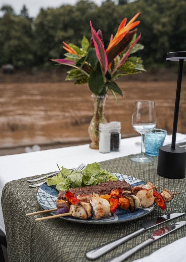 Grilled meat and vegetable skewers served riverside at The Namkhan restaurant in Luang Prabang, featuring tropical flowers and river views