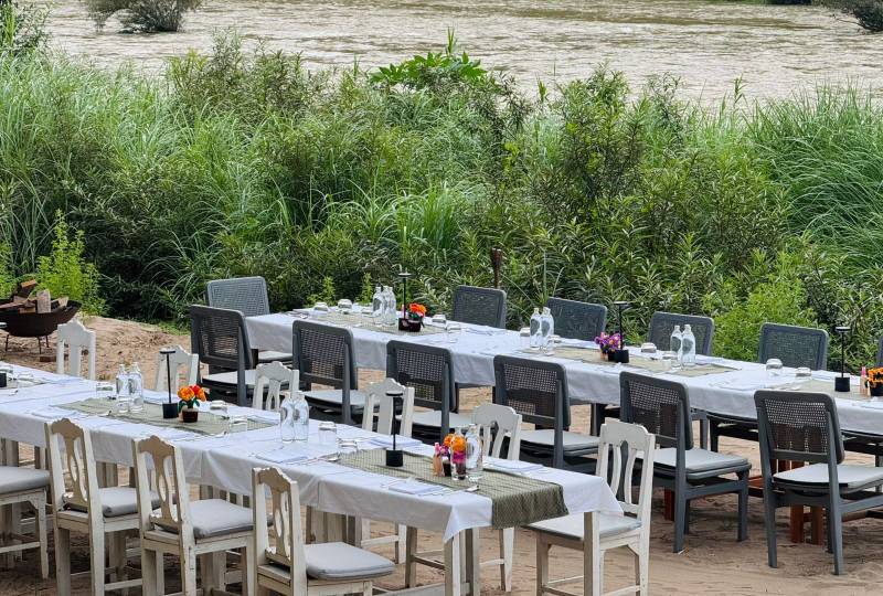 Long communal dining tables set for group event along the Nam Khan river at The Namkhan resort in Luang Prabang, Laos with natural vegetation.