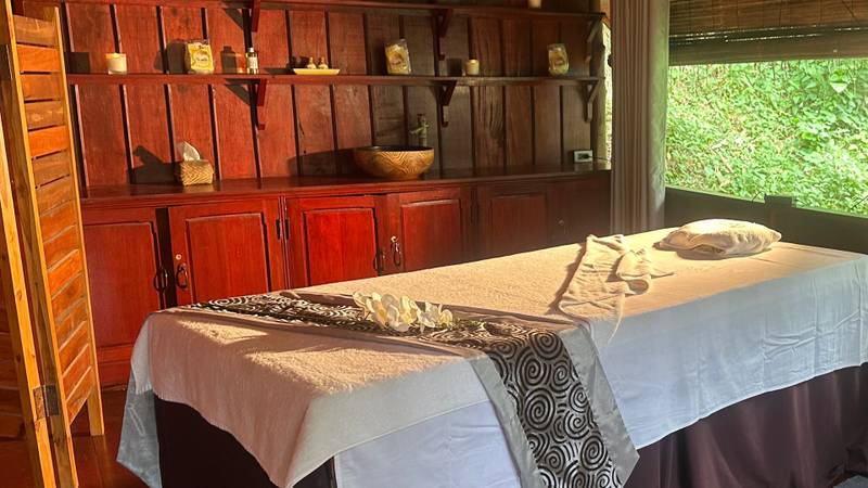Tranquil spa treatment room at The Namkhan in Luang Prabang featuring traditional wooden decor, massage table, and jungle views through window
