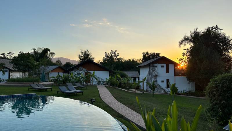 Infinity pool with sun loungers overlooking traditional Lao villas and manicured gardens during sunset at Namkhan resort, Luang Prabang