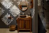 Teak vanity with ceramic basin and damask wallpaper in a bathroom at The Namkhan, Luang Prabang, blending traditional Lao craft with modern comfort