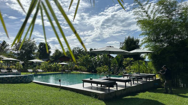 Emerald pool with dark wood loungers and white umbrellas surrounded by tropical gardens at The Namkhan resort in Luang Prabang, Laos