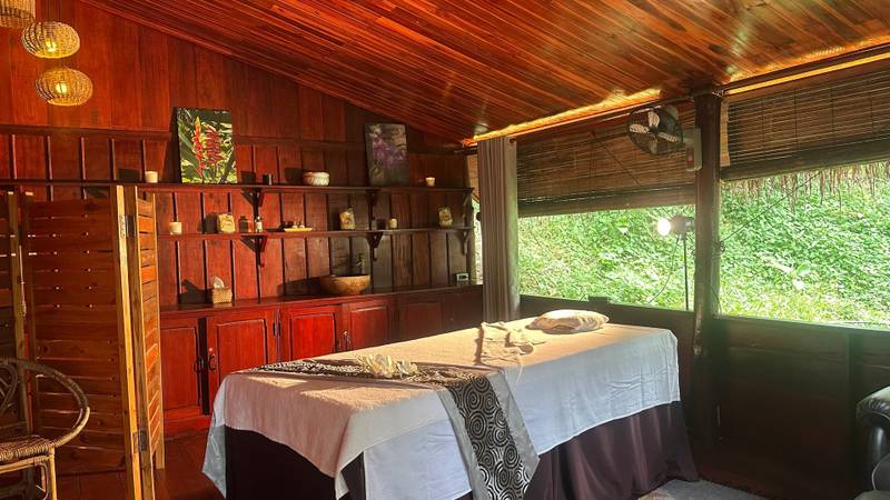 Traditional spa treatment room with twin massage tables at The Namkhan resort in Luang Prabang, featuring warm teak wood interiors and garden views
