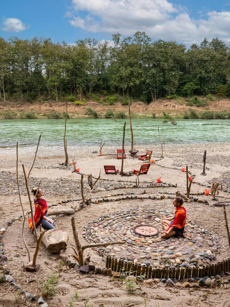 Guests meditating in a riverside stone circle at The Namkhan resort with the Nam Khan River and tropical forest in Luang Prabang, Laos