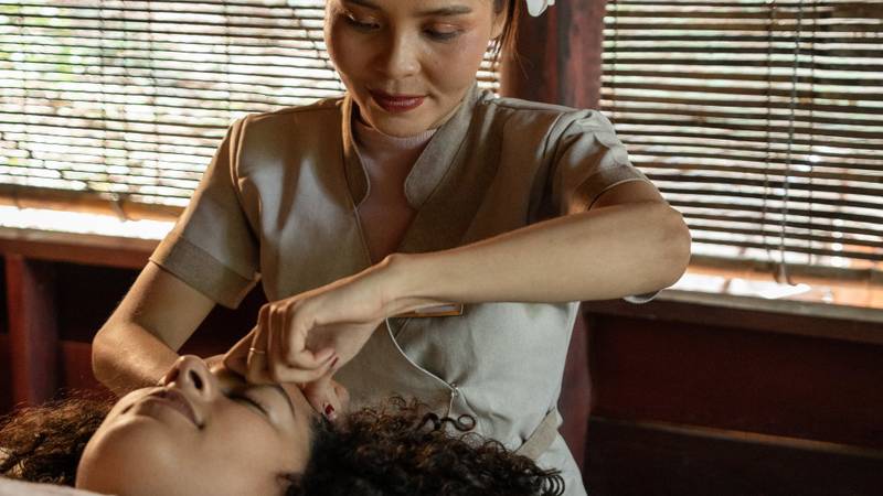 Guest receiving a therapeutic facial massage at The Namkhan spa in Luang Prabang, with traditional wooden blinds and natural light