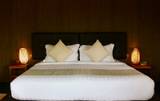 Inviting guest room bed at The Namkhan in Luang Prabang, featuring crisp white linens, neutral cushions, and warm bamboo bedside lamps.