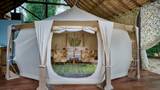 Interior of a canvas glamping tent with floral armchairs, small table, and bed.