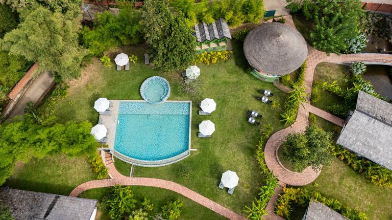 Aerial view of The Namkhan resort pool surrounded by lush gardens and traditional thatched-roof villas in Luang Prabang, Laos
