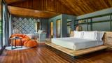 Spacious villa bedroom with teak ceiling, low platform bed, and open wardrobe area.