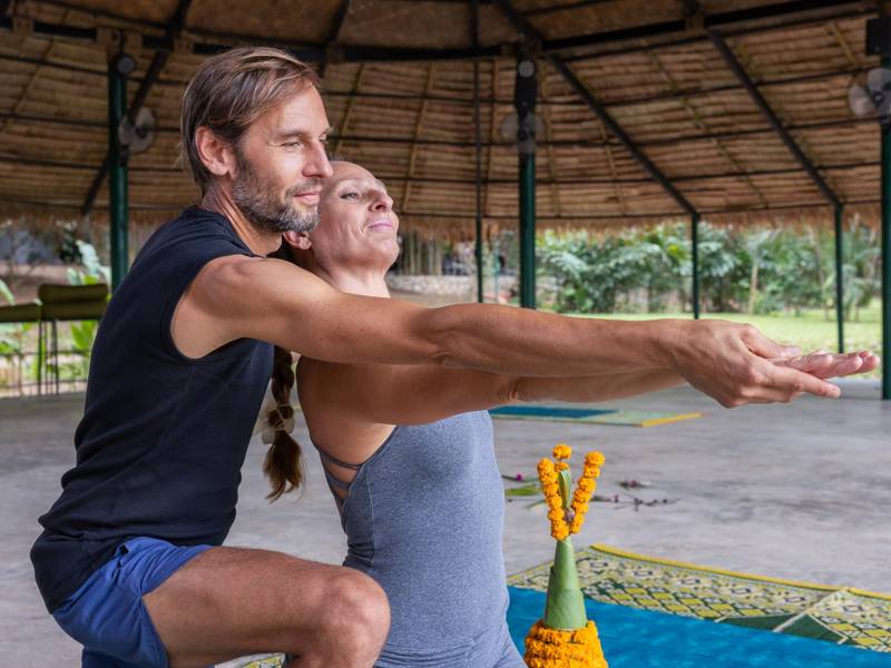Private yoga instruction session at The Namkhan wellness pavilion in Luang Prabang, featuring traditional thatched architecture and garden views