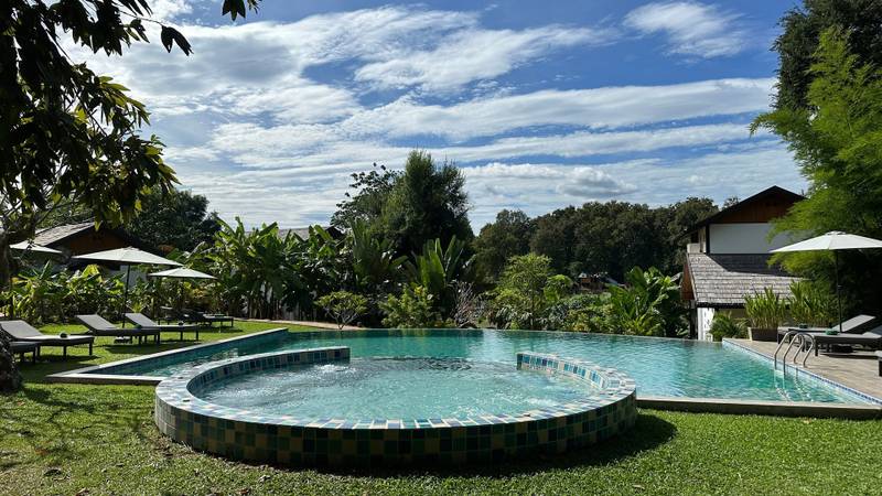 The Namkhan infinity pool surrounded by tropical gardens and traditional Lao architecture in Luang Prabang, featuring mosaic tile details and loungers.