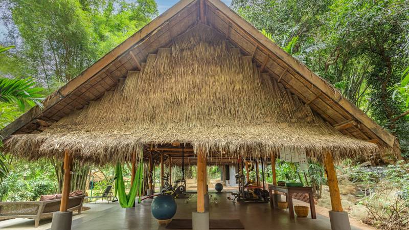 Open-air fitness pavilion with thatched roof and exercise equipment surrounded by tropical greenery at The Namkhan resort in Luang Prabang, Laos