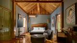 Spacious hotel suite with vaulted teak ceiling, live-edge wooden headboard, and muted grey walls.