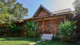 A traditional teak wood guesthouse building surrounded by tropical garden greenery and banana palms.