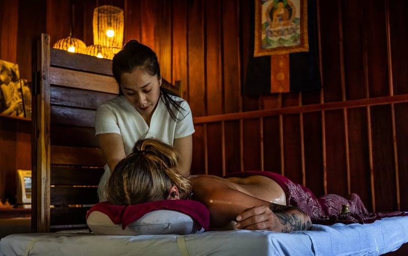Professional therapist providing traditional Lao massage in the warm, bamboo-accented spa at The Namkhan resort in Luang Prabang, Laos.
