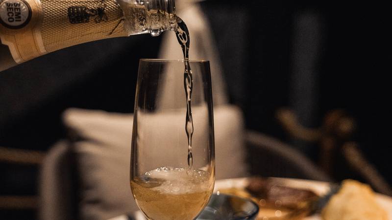Champagne being poured into flute glass at The Namkhan restaurant table setting with gourmet dishes in Luang Prabang, Laos