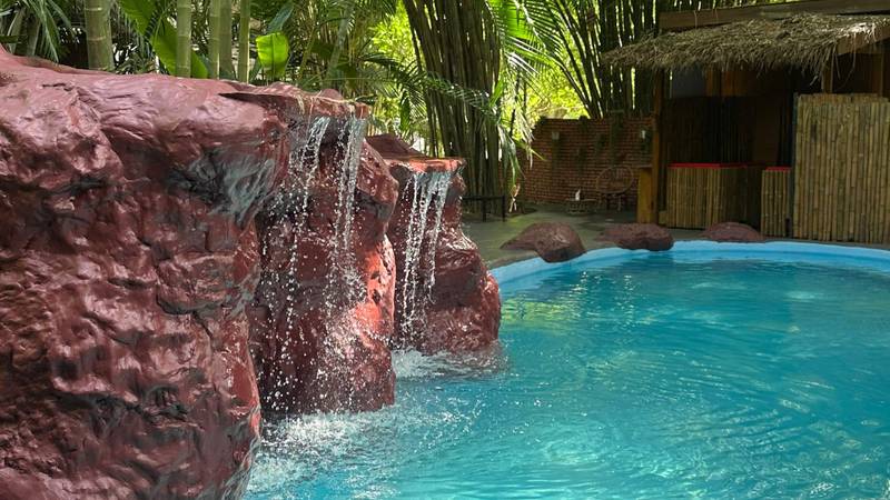 Turquoise pool with cascading waterfall feature surrounded by bamboo and tropical palms at The Namkhan resort in Luang Prabang, Laos