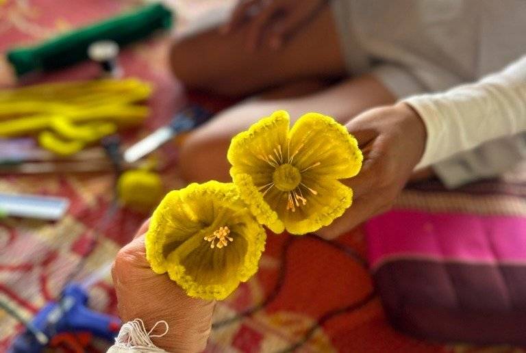 Guest crafting vibrant yellow marigold flower offerings during a cultural workshop at The Namkhan, Luang Prabang, surrounded by colorful fabrics