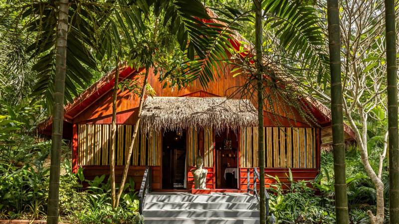 Traditional teak garden villa with thatched roof and private terrace at The Namkhan resort, nestled in lush tropical gardens in Luang Prabang, Laos.