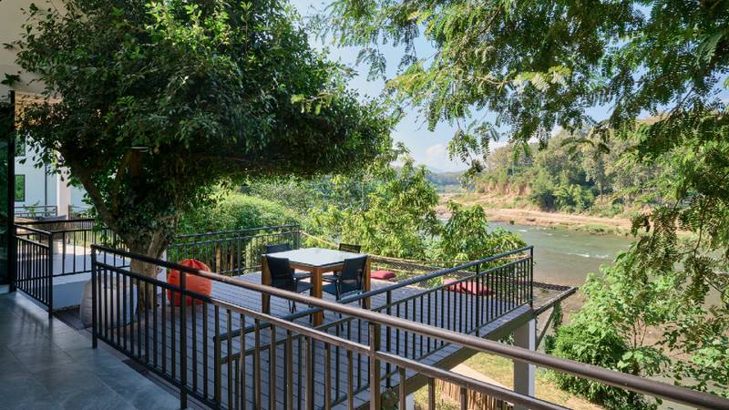 A furnished balcony terrace overlooks the Namkhan River surrounded by dense green trees.