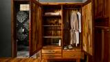 Open teak wardrobe with folded towels, hanging robes, and guest slippers inside.
