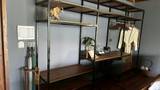 Open steel and teak shelving unit with carved elephant figurine and glassware inside a hotel room.