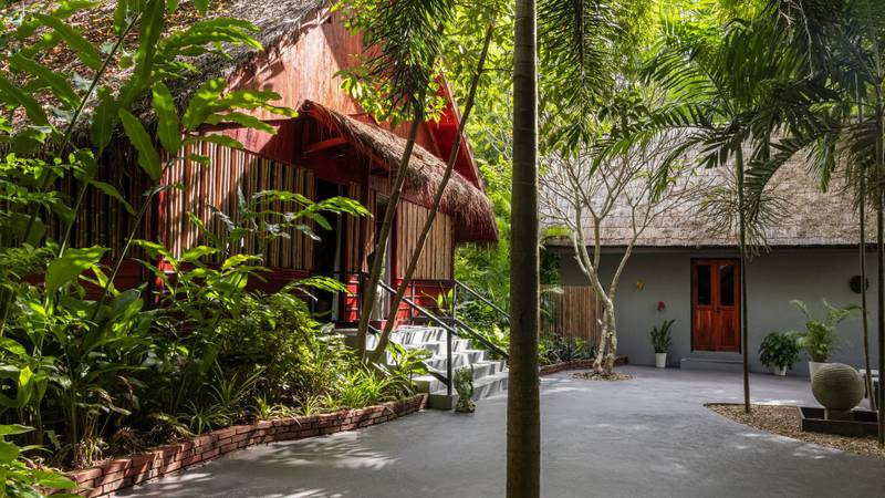 Traditional thatched-roof villa along garden pathway at The Namkhan resort in Luang Prabang, surrounded by tropical palms and native plantings
