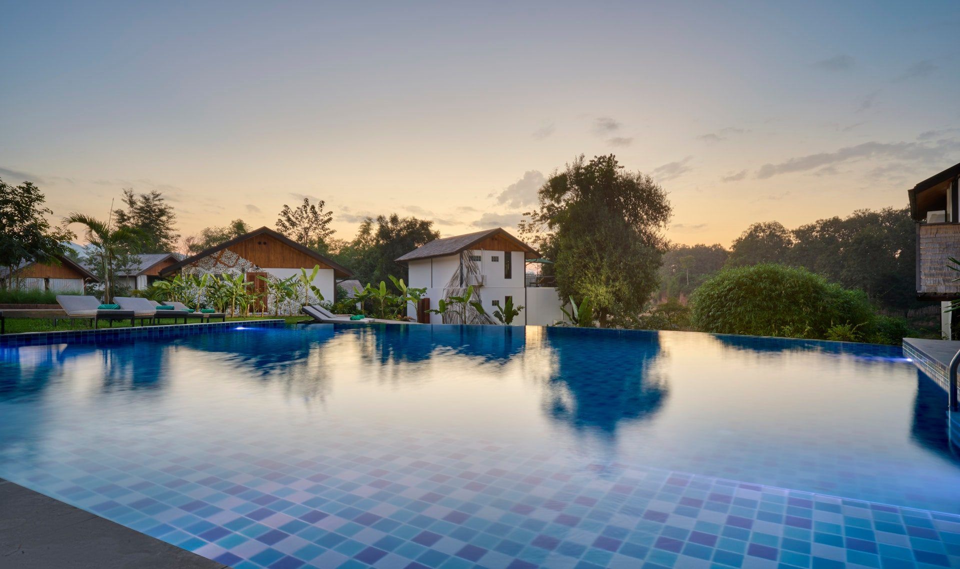 Infinity pool at The Namkhan resort reflecting golden sunset sky with traditional Lao villas and tropical gardens in Luang Prabang, Laos