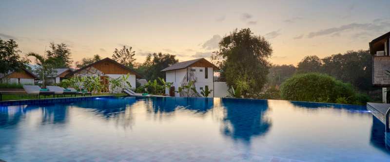 Infinity pool at The Namkhan resort reflecting golden sunset sky with traditional Lao villas and tropical gardens in Luang Prabang, Laos