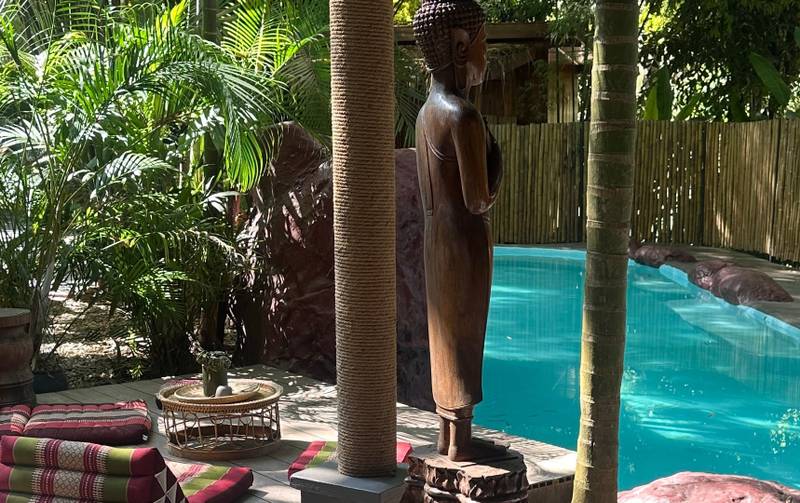 Private pool pavilion with traditional wooden sculpture and triangle cushions at The Namkhan resort in Luang Prabang, surrounded by lush tropical gardens