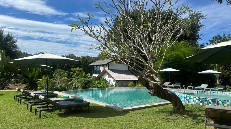 Infinity pool with sun loungers and umbrellas surrounded by lush tropical gardens at The Namkhan resort in Luang Prabang, Laos