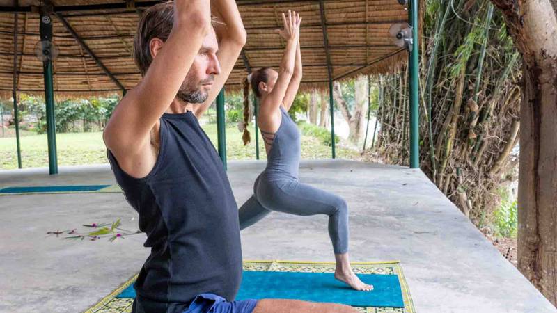 Guests practicing yoga in the open-air pavilion at The Namkhan resort, surrounded by tropical gardens in Luang Prabang, Laos.