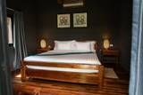 Guest room with wooden bed frame, white linens, and traditional artwork at The Namkhan resort in Luang Prabang, featuring warm ambient lighting.